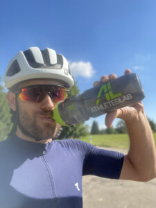 Radfahrer mit Helm und Sonnenbrille trinkt aus einer Trinkflasche