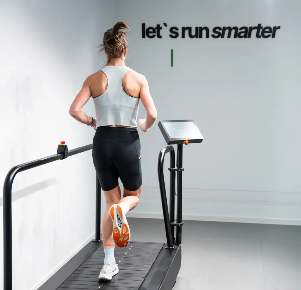 Läuferin von hinten auf dem Laufband, an der Wand der Schriftzug let's run smarter